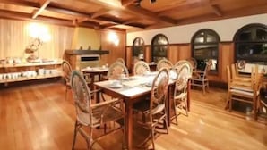 A dining area with wooden tables and chairs, a kitchen in the background, and arched windows. - Campos Hotel do Sol (Campos do Jordão)