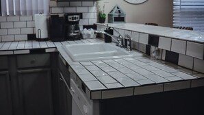 Una cocina moderna con una isla grande, azulejos tipo metro blancos, armarios oscuros, horno empotrado e iluminación colgante.