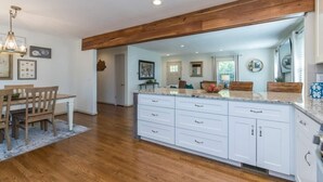 A modern kitchen with white cabinets, a wooden ceiling, and a dining area with a table and chairs.