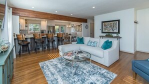 A spacious living room with a white sofa, a coffee table, and a kitchen area with wooden bar stools.