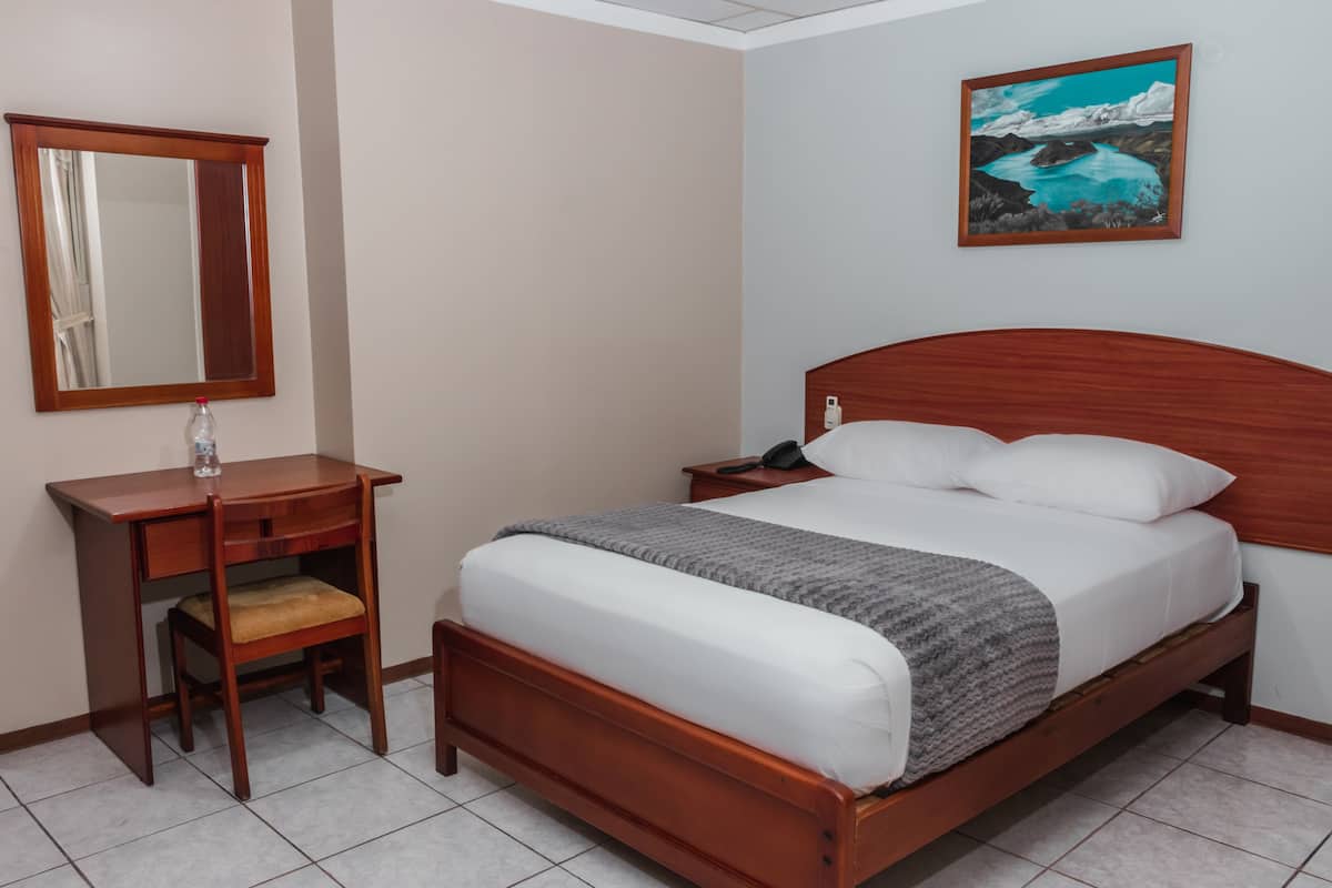Quarto bem arrumado com cama de madeira, mesa de cabeceira, espelho e um quadro na parede.
