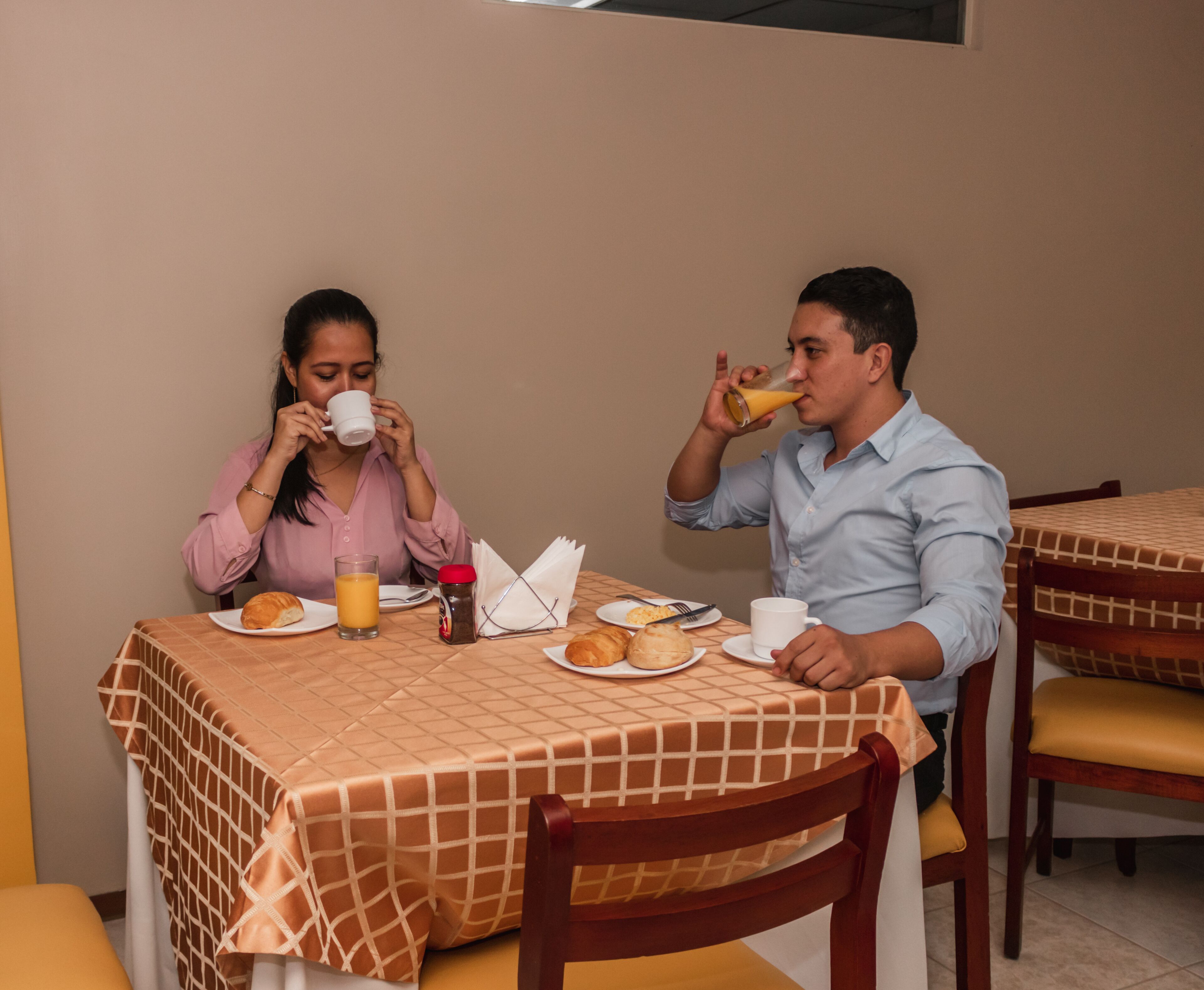 A dining area with a table set for two, featuring a checkered tablecloth, plates with food, and drinks.