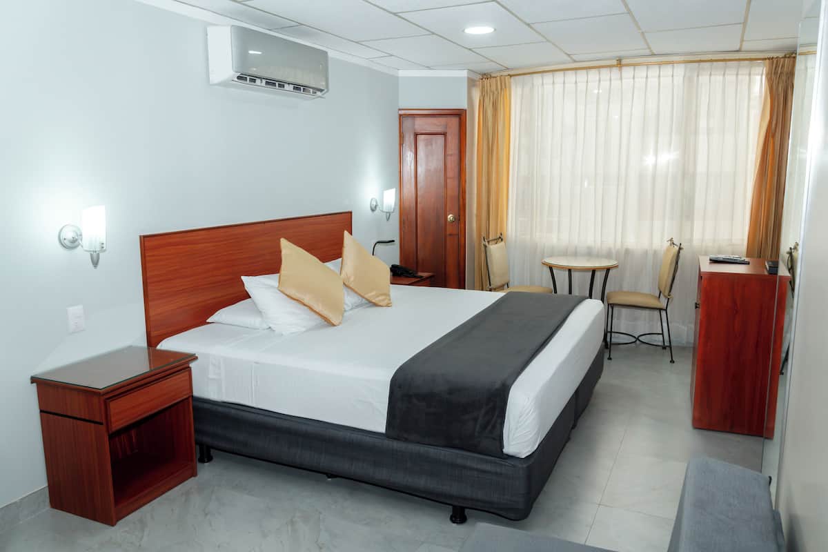 Quarto de hotel com uma cama grande, mesas de cabeceira, escrivaninha, cadeira e guarda-roupa.