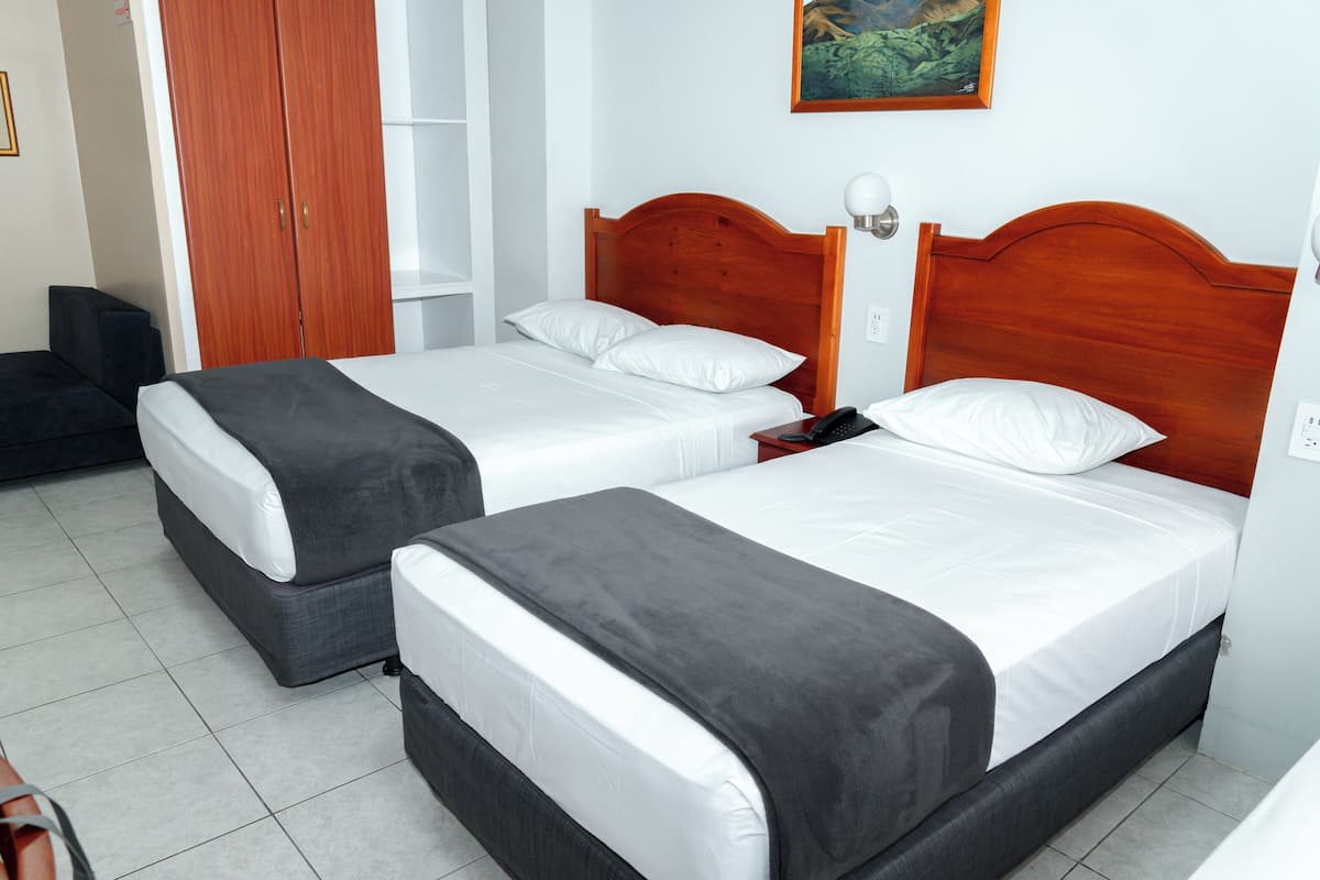 Duas camas de solteiro com cabeceiras de madeira, roupa de cama branca e mantas cinzentas num quarto com soalho em mosaico.