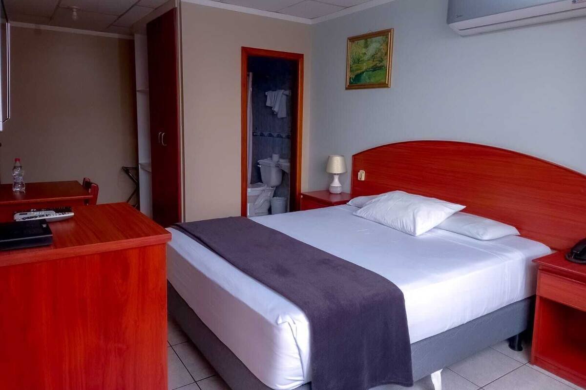 Quarto de hotel com cama, mesa de cabeceira e escrivaninha com cadeira.