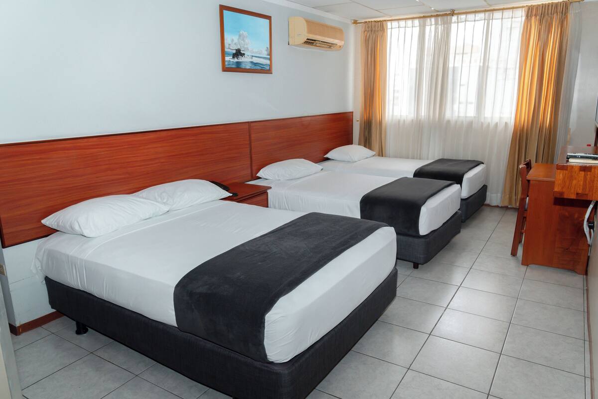 Quarto de hotel com duas camas, cabeceira de madeira, um quadro na parede e uma janela com cortinas.