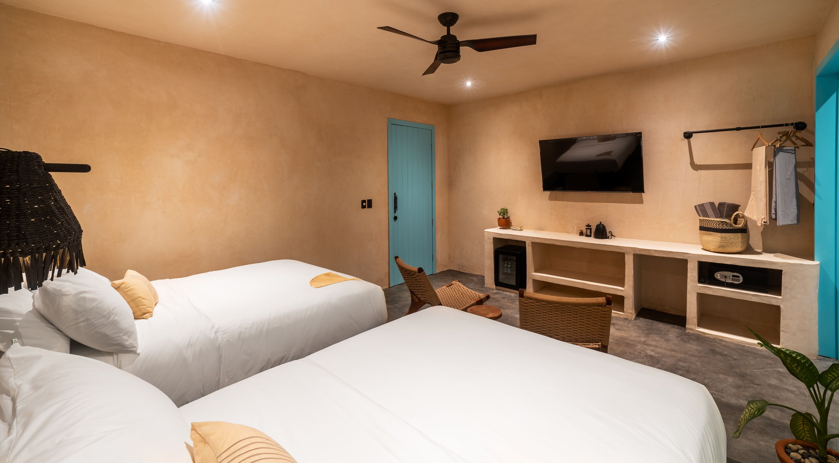 Habitación de hotel con dos camas, televisor, escritorio con computadora y ventilador de techo.