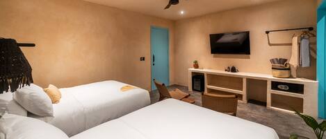 Habitación de hotel con dos camas, televisor, escritorio con computadora y ventilador de techo.