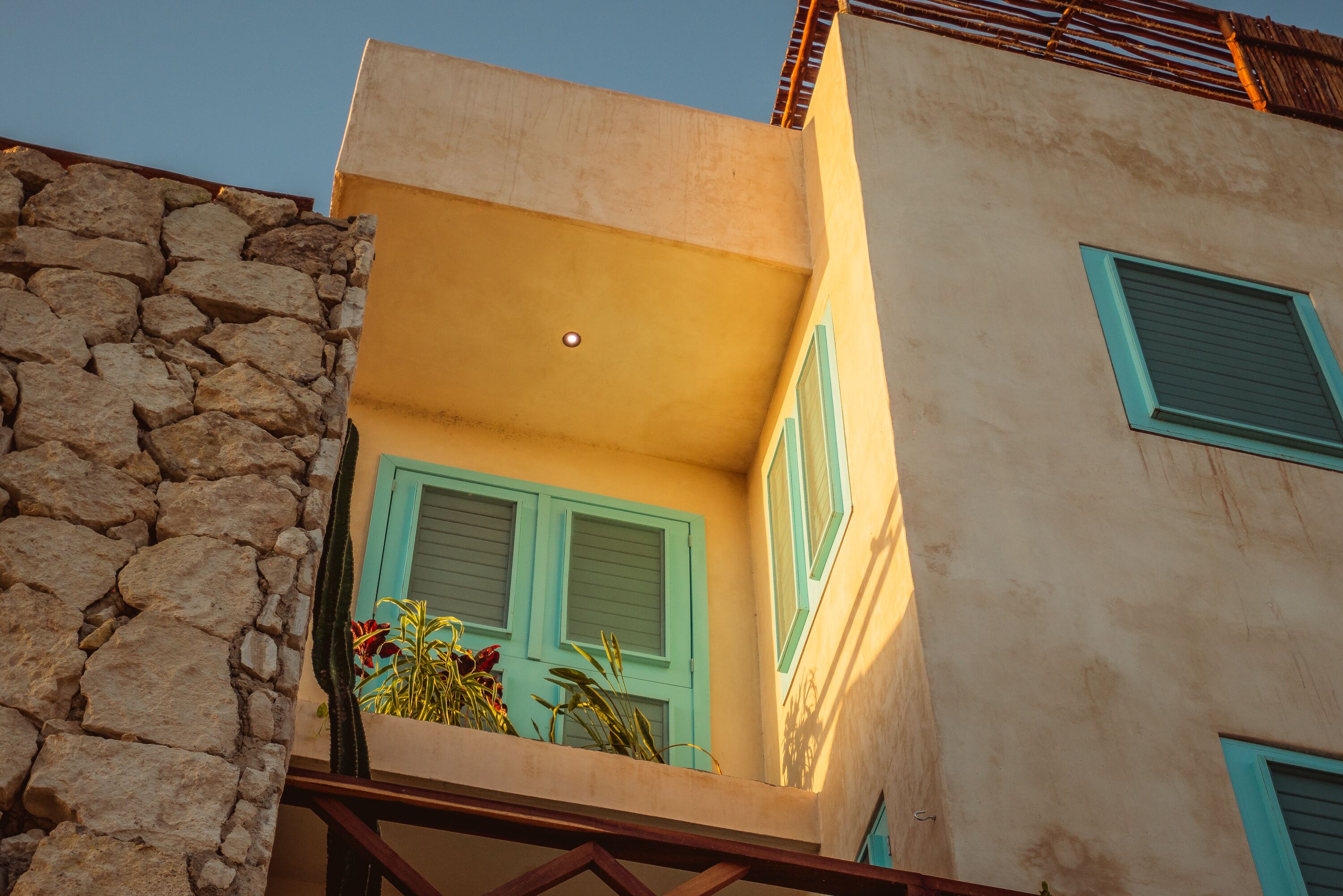 A building with a stone facade, a balcony with green shutters, and a small window with a shutter.