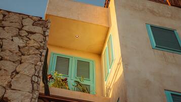 A building with a stone facade, a balcony with green shutters, and a small window with a shutter.