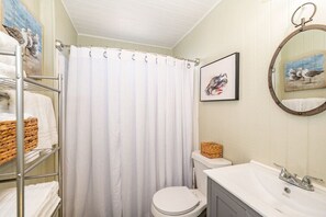 Een badkamer met een witte douchegordijn, een wit toilet, een wastafel met spiegel en kunstwerken aan de muur.