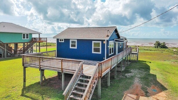 Una casa azul con terraza de madera y escaleras que llevan a un balcón.