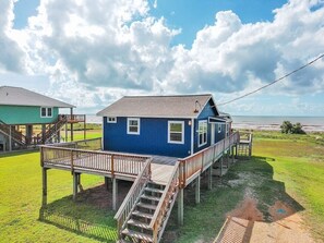 Een blauw huis met een houten terras en een trap naar een balkon.