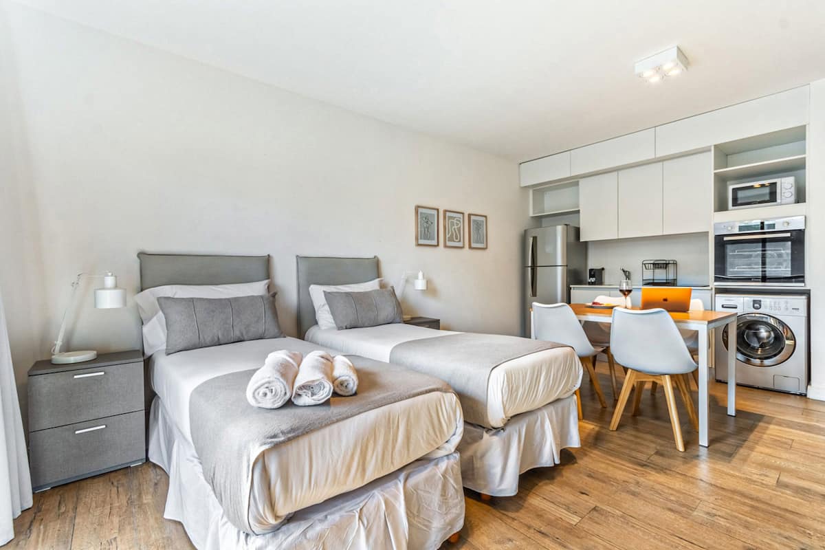 A modern hotel room with two beds, a desk, and a washing machine.
