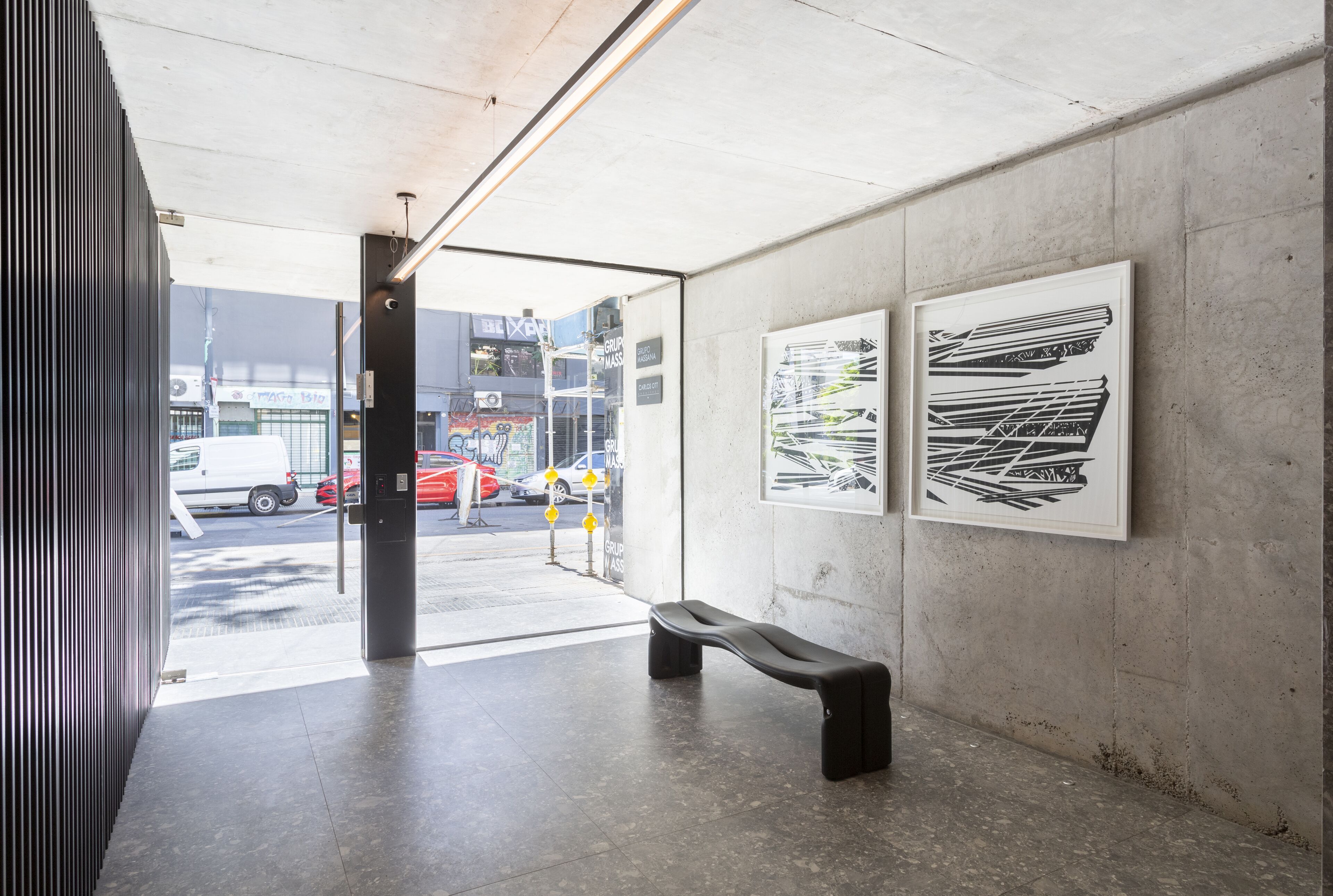 Um espaço interno com um banco, paredes de concreto e duas obras de arte emolduradas.