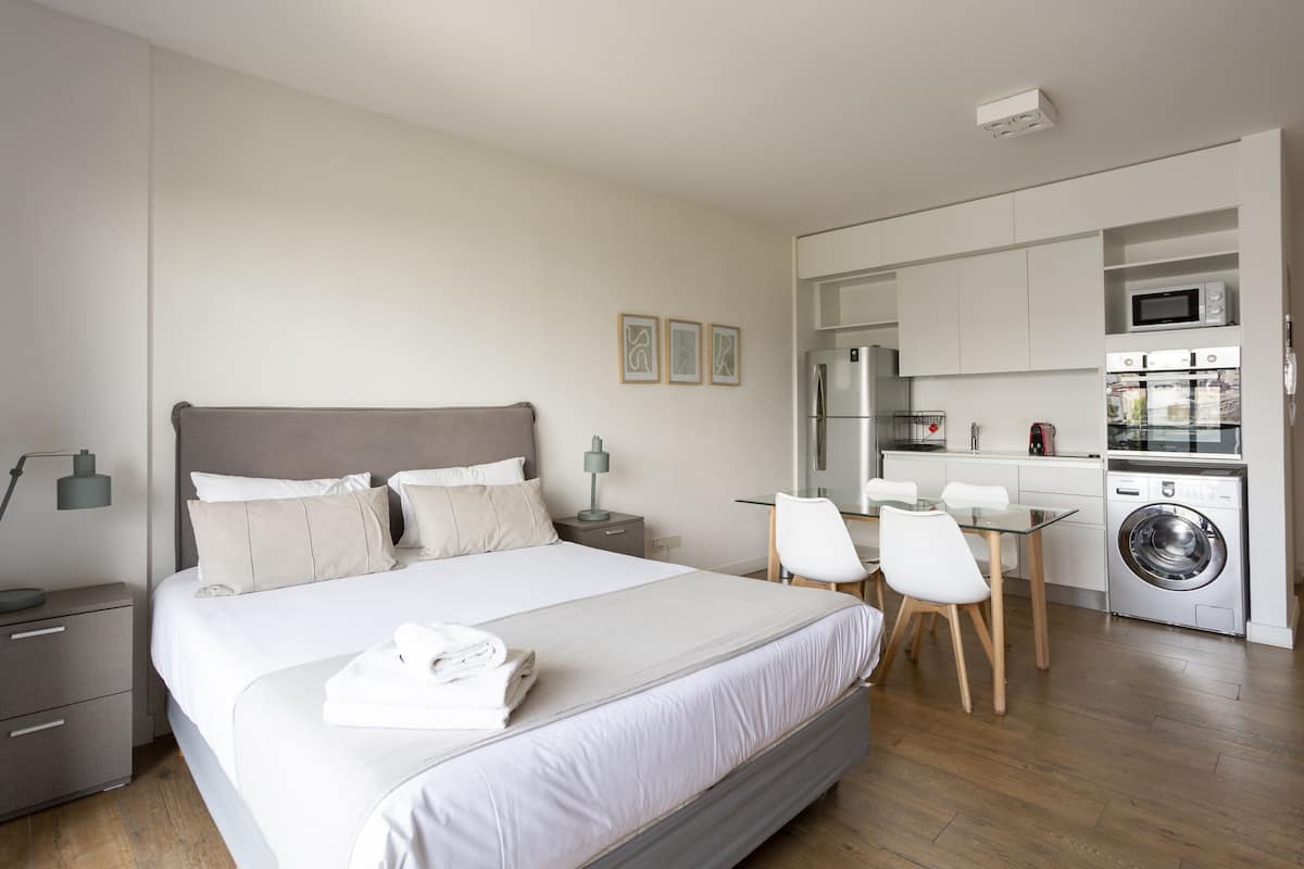 A modern bedroom with a large bed, bedside tables, a desk, and a washing machine.