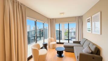 A modern living room with large windows, a sofa, a round table, and two armchairs.