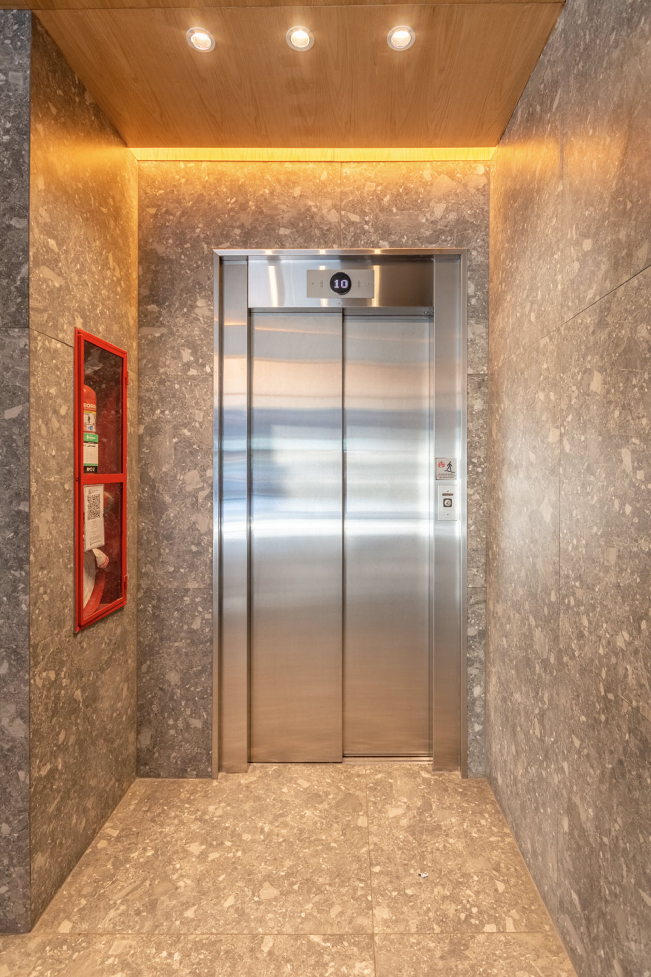 An elevator with a metallic finish, a digital display, and a fire extinguisher mounted on the wall.