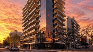 Un moderno edificio de rascacielos con varios balcones, fachada de vidrio y un cielo al atardecer.