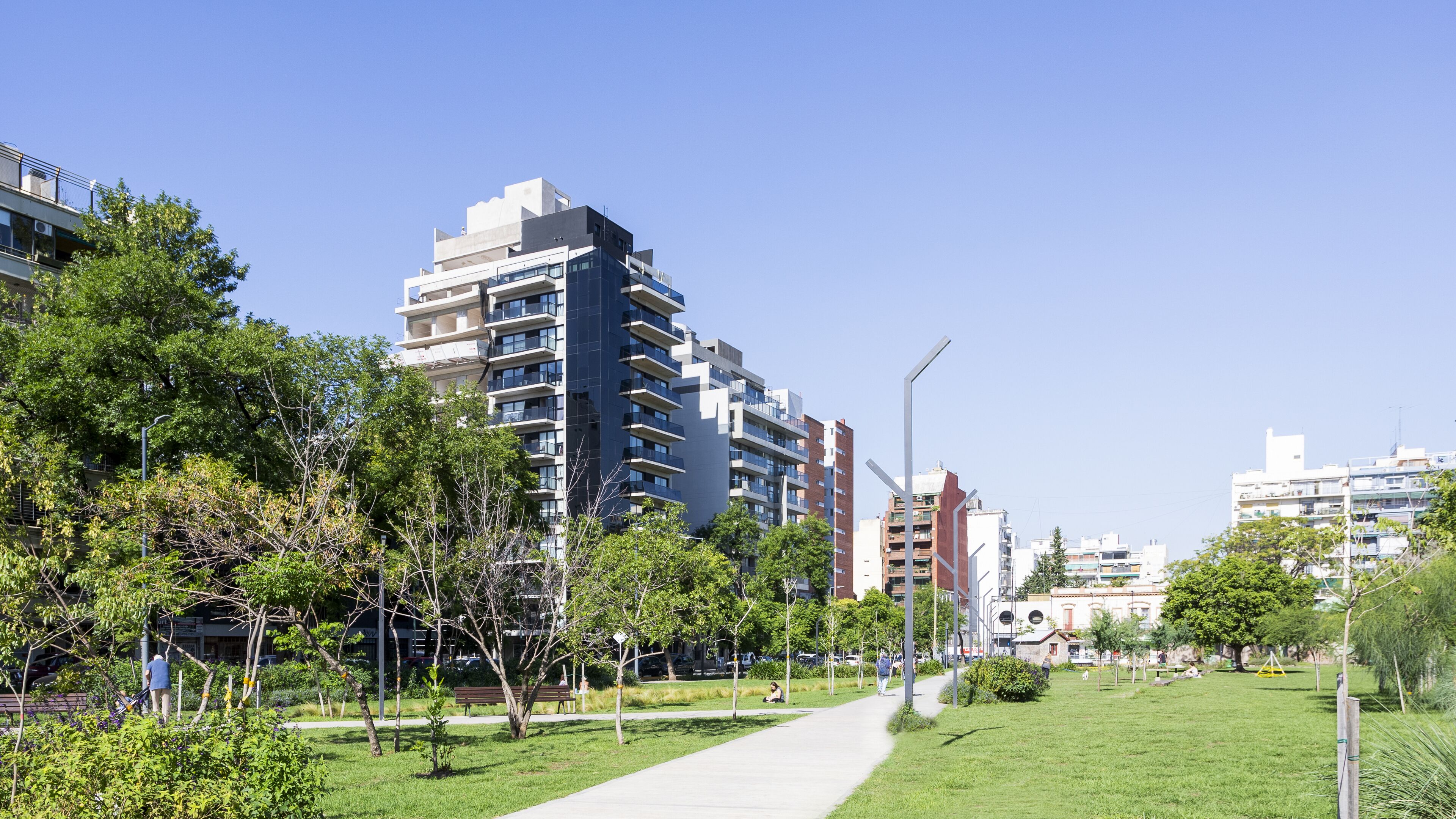 A modern urban area with a pathway, green spaces, and multi-story residential buildings.