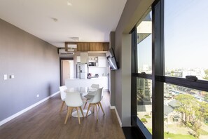 A modern kitchen with white cabinets, a dining area with a glass table and white chairs, and a large window offering a city view. - Live Belgrano Boutique Apartments (Buenos Aires)