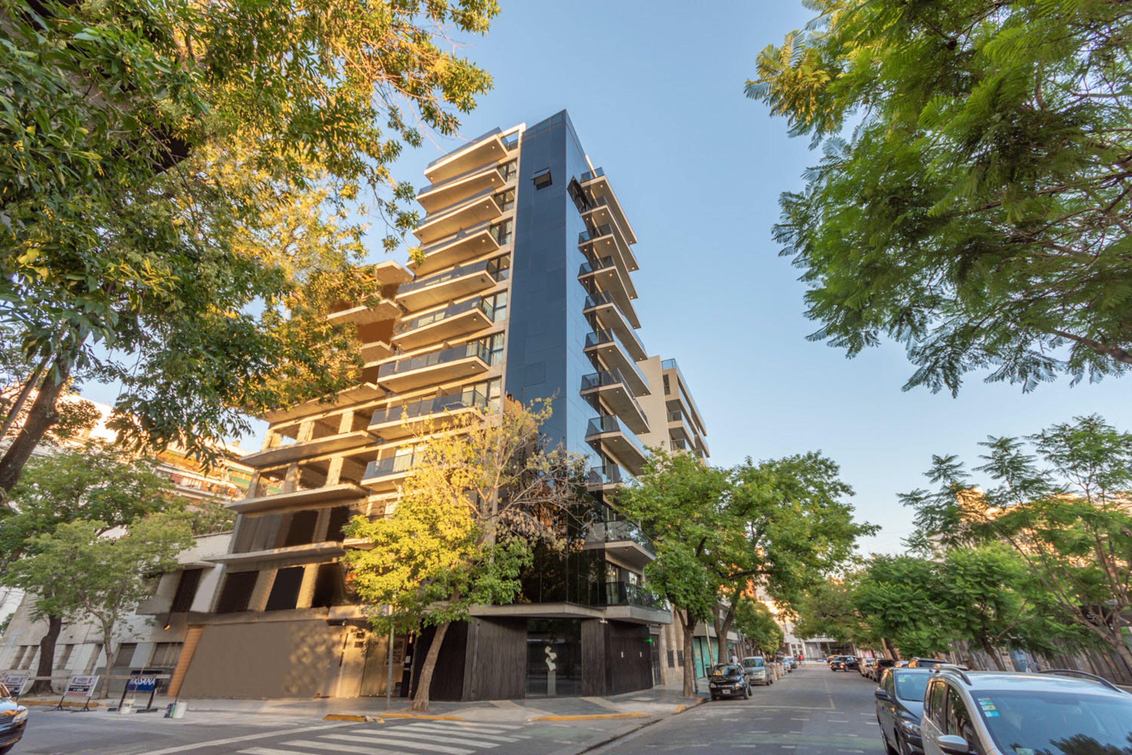 A modern multi-story building with a unique architectural design, surrounded by trees and parked cars.