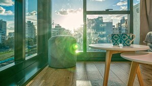 Una habitación con un amplio ventanal que ofrece vistas de la ciudad, una mesa redonda de madera y dos tazas estampadas sobre la mesa.