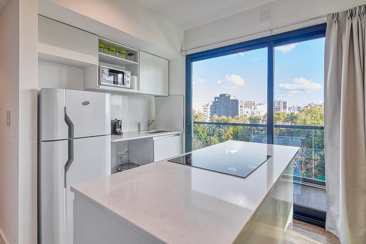 A modern kitchen with a large island, built-in microwave, and a view of a cityscape through a large window.