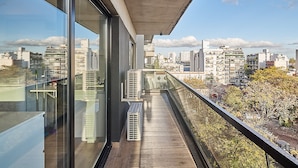 Un balcón moderno con vistas a la ciudad, ventanas amplias y unidades de aire acondicionado.