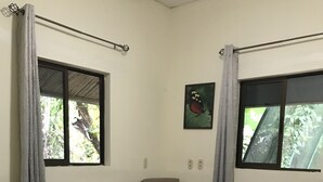 Una stanza con un letto, una sedia, due finestre e un quadro appeso al muro.