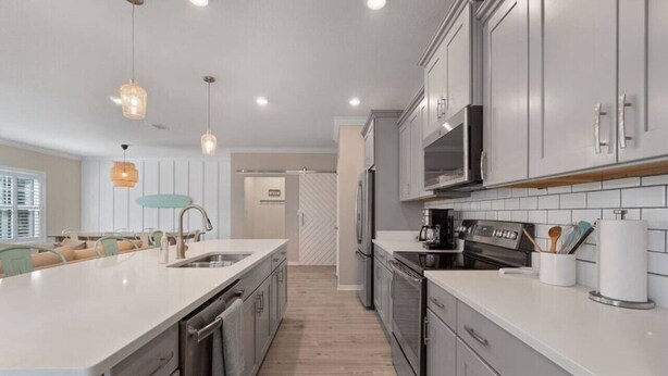 A modern kitchen with white cabinetry, stainless steel appliances, and pendant lighting. - 4BR, free shuttle, gym, pool, BBQ, beach access (Pensacola)