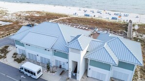 A coastal building with a metal roof, adjacent to a sandy beach with umbrellas and lounge chairs. - 4BR, free shuttle, gym, pool, BBQ, beach access (Pensacola)