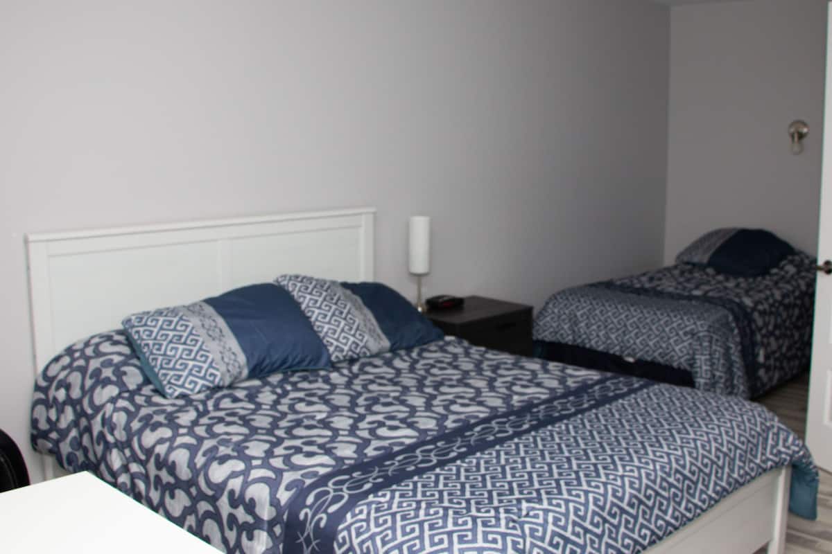 A bedroom with two beds, a bedside table, and a door.