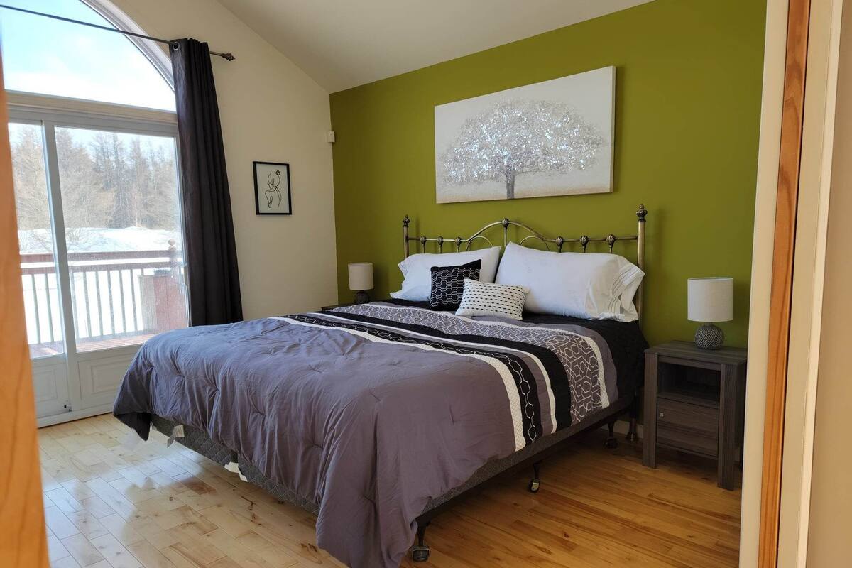 A bedroom with a bed, a nightstand, a lamp, a painting, and a window with curtains.