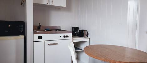 A compact kitchen with white cabinets, a stove, a microwave, and a coffee maker. There is a small table with two white chairs.