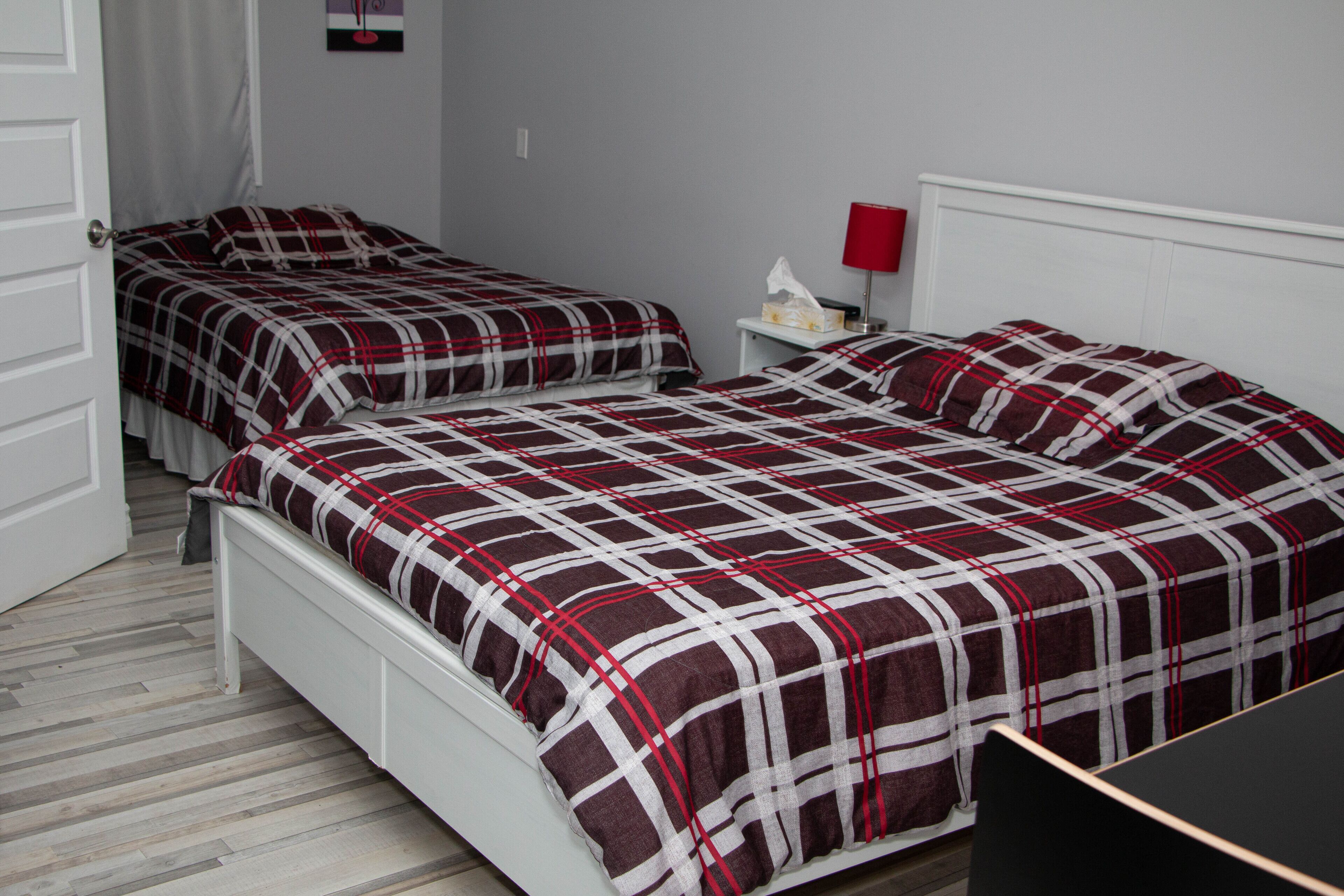 A room with two beds, each with a plaid bedspread, a nightstand with a lamp, and a small table.