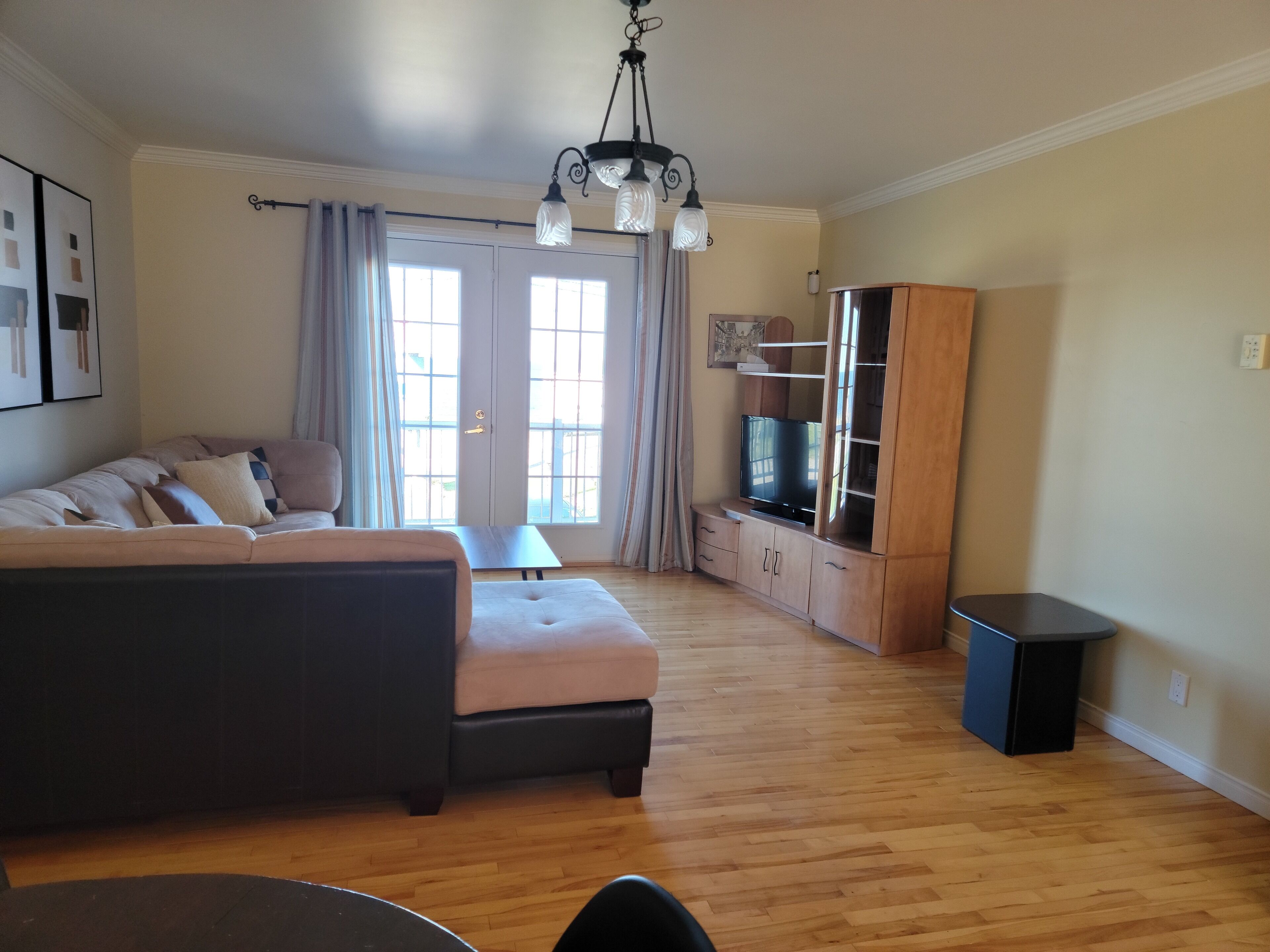 A living room with a sofa, ottoman, wooden cabinet, and a television.