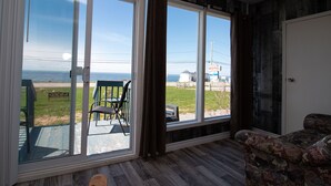 Una habitación con un gran ventanal corredizo que da a una terraza con sillas y vistas al océano, con un letrero de motel a lo lejos.