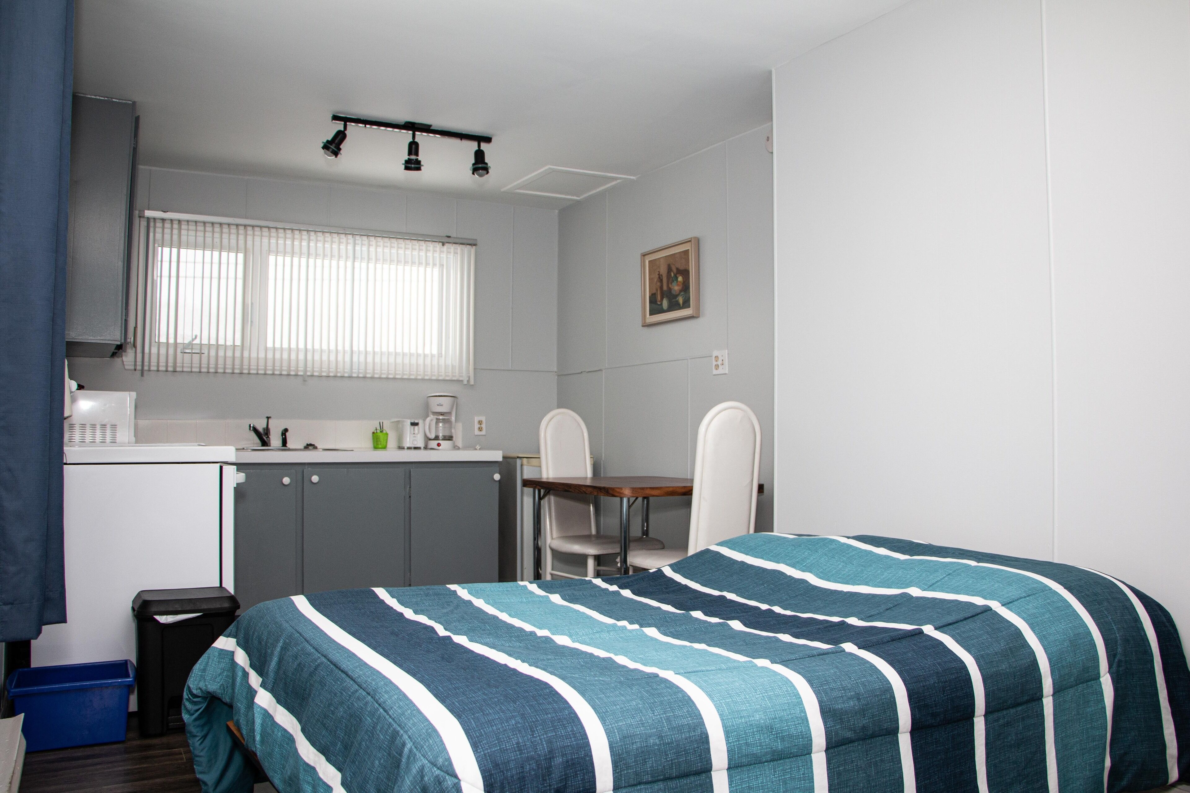 Habitación compacta con cama, pequeña kitchenette, comedor y ventana con persianas.