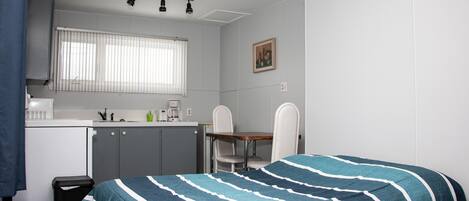 Habitación compacta con cama, pequeña kitchenette, comedor y ventana con persianas.