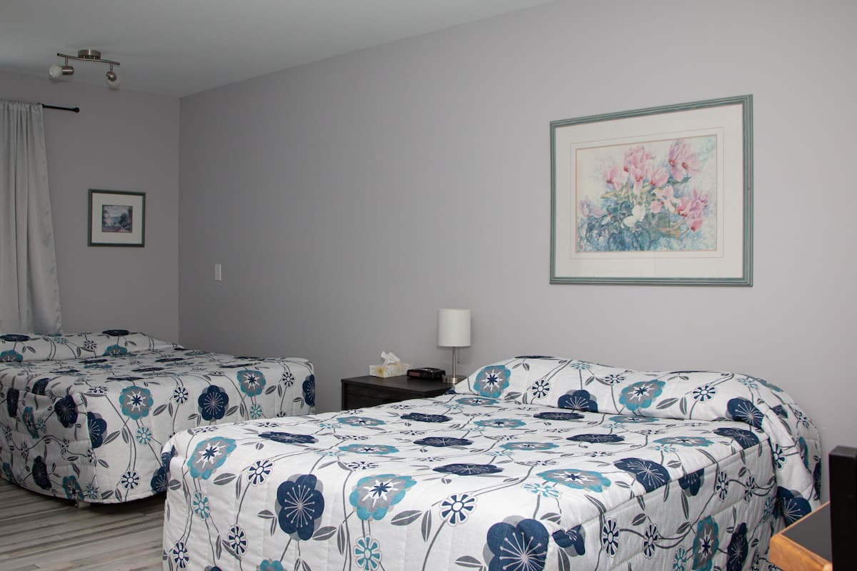A hotel room with two beds, a nightstand, a lamp, and a framed floral artwork on the wall.