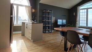 Una cocina moderna con una isla central, un comedor con mesa y sillas de madera, y ventanas amplias que ofrecen vistas.