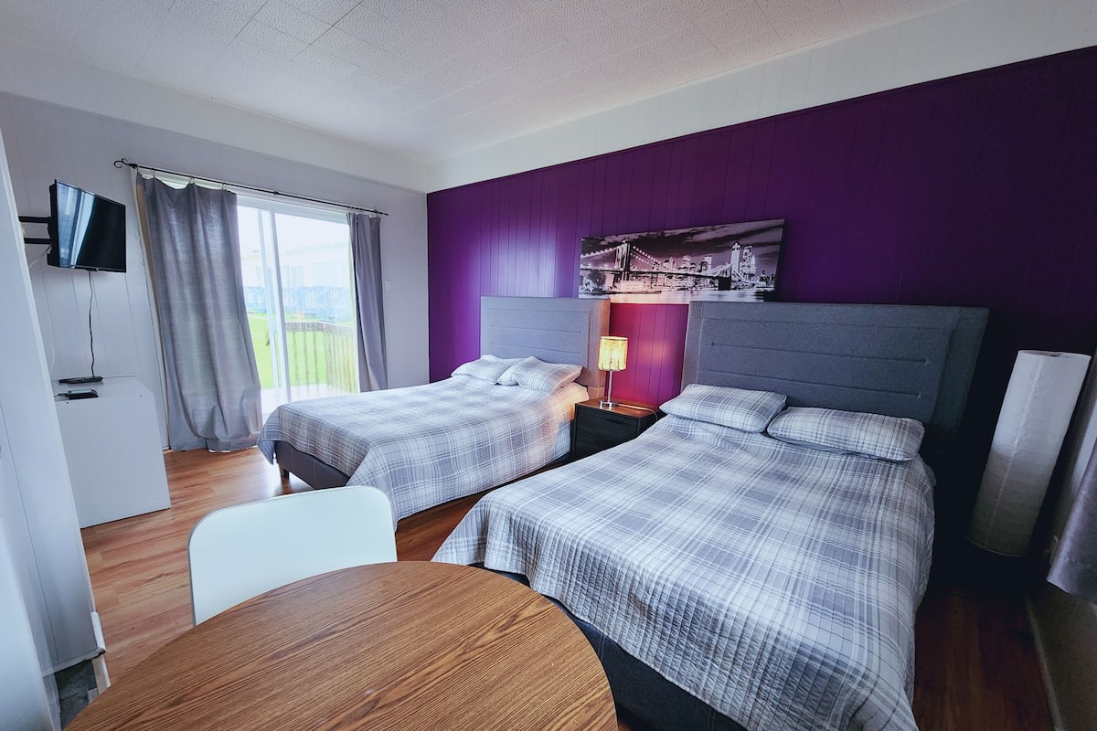 A hotel room with two beds, a TV, a table, and a window with curtains.