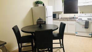 Una cocina compacta con armarios blancos, una estufa y una mesa de comedor con cuatro sillas.