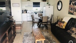 Una sala de estar moderna con un sofá negro, una mesa de centro de madera y una zona de comedor con una mesa y sillas blancas.