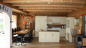 A cozy cabin interior with a wooden ceiling, a dining area with a table and chairs, a kitchen with white cabinets, and a fireplace. - Cozy vacation apartment directly on the fjord (Sørbøvågen)