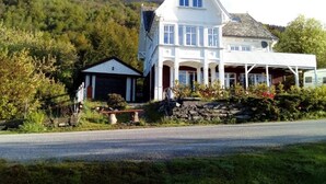 A large, white, two-story house with a steeply pitched roof, a stone foundation, and a covered porch. - Cozy vacation apartment directly on the fjord (Sørbøvågen)