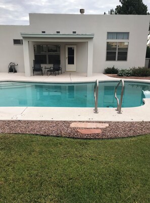 A modern house with a swimming pool, a covered patio with chairs, and a well-maintained lawn.