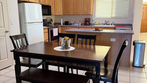 Une cuisine avec des meubles de rangement en bois, un réfrigérateur blanc, une table à manger avec des chaises et un luminaire suspendu.