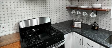 A modern kitchen with a stainless steel stove, oven, and a range hood. There are white cabinets, a granite countertop, and a backsplash with a geometric pattern.